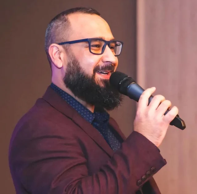 Andrei Dumitrașcu cântând la microfon, în sacou vișiniu